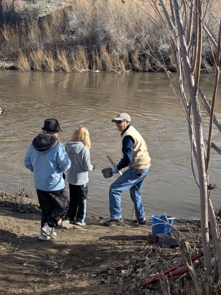 Two students and a volunteer release trout into a river